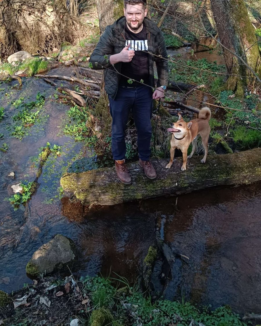 Maksim mit seinem Hund auf einem Baumstamm ueber einem Bach